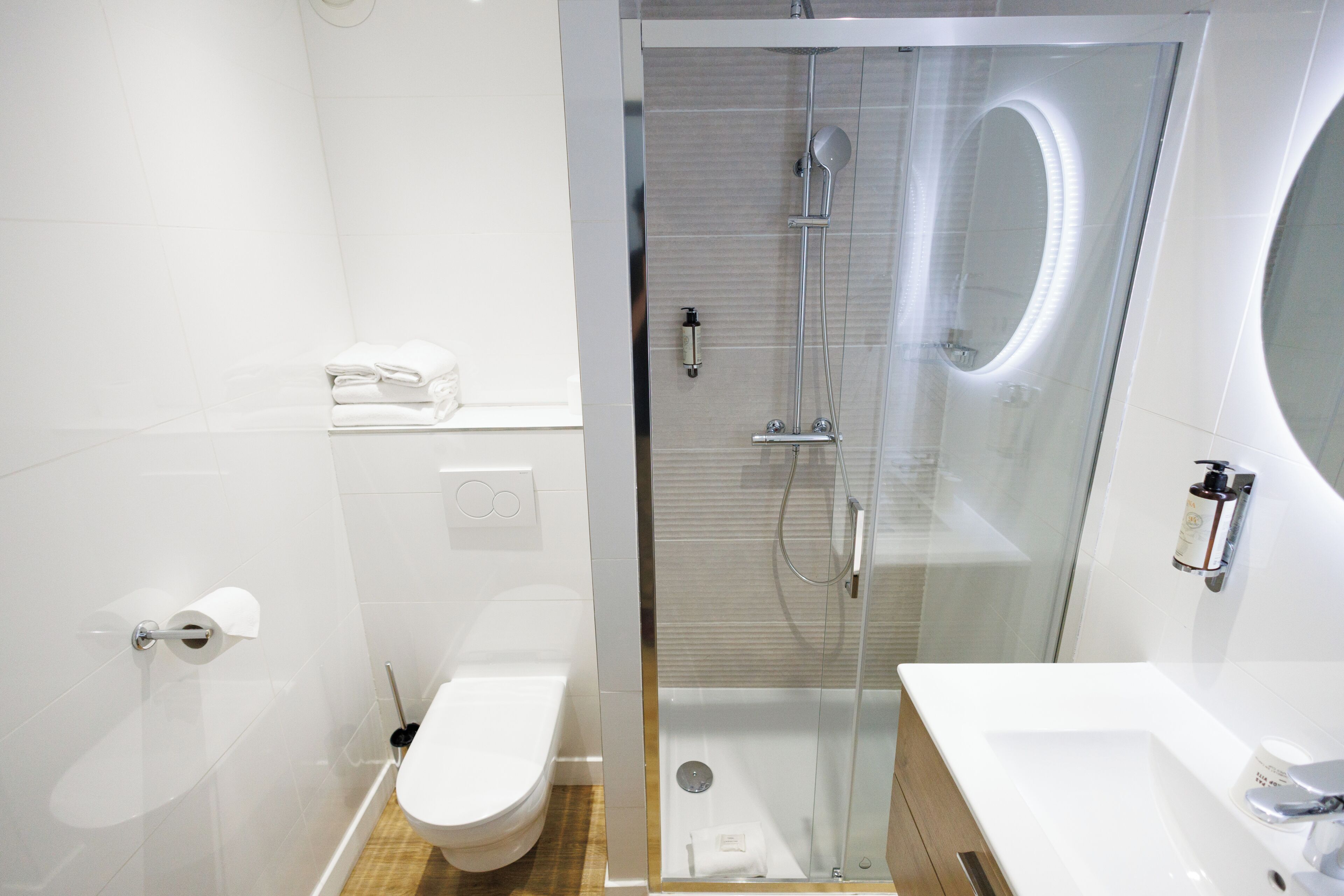 A modern bathroom with a glass-enclosed shower, a white toilet, and a sink with a mirror.
