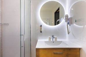 Un baño moderno con cabina de ducha de vidrio, un espejo redondo, un lavabo blanco y un mueble de tocador de madera.