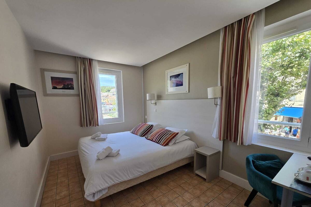 Une chambre d’hôtel avec un lit, un bureau, une chaise, une télévision et une fenêtre avec des rideaux.