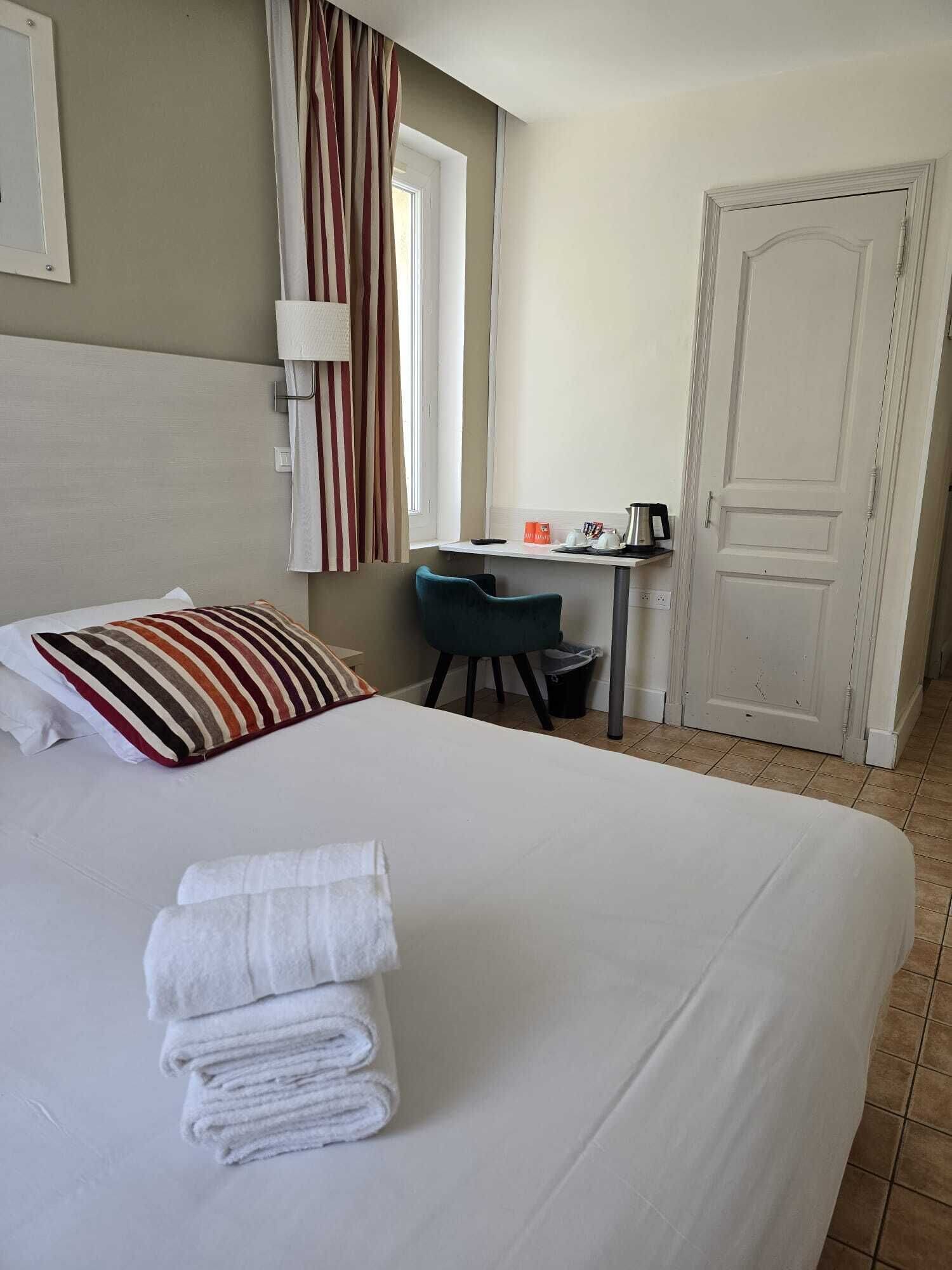 Habitación de hotel con cama, escritorio, silla, ventana con cortinas y puerta.