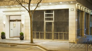 A hotel entrance with a large glass door, potted plants, and a clear view of the interior. - Telioni (Thessaloniki)