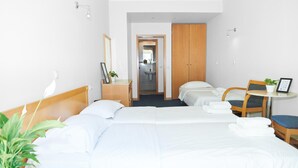 A hotel room with two beds, a desk, a chair, a small table, a potted plant, and a bathroom visible through an open door. - Telioni (Thessaloniki)