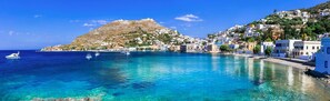 A coastal town with clear blue waters, a hill with buildings, and a boat in the sea. - Galini Hotel (Aegina)