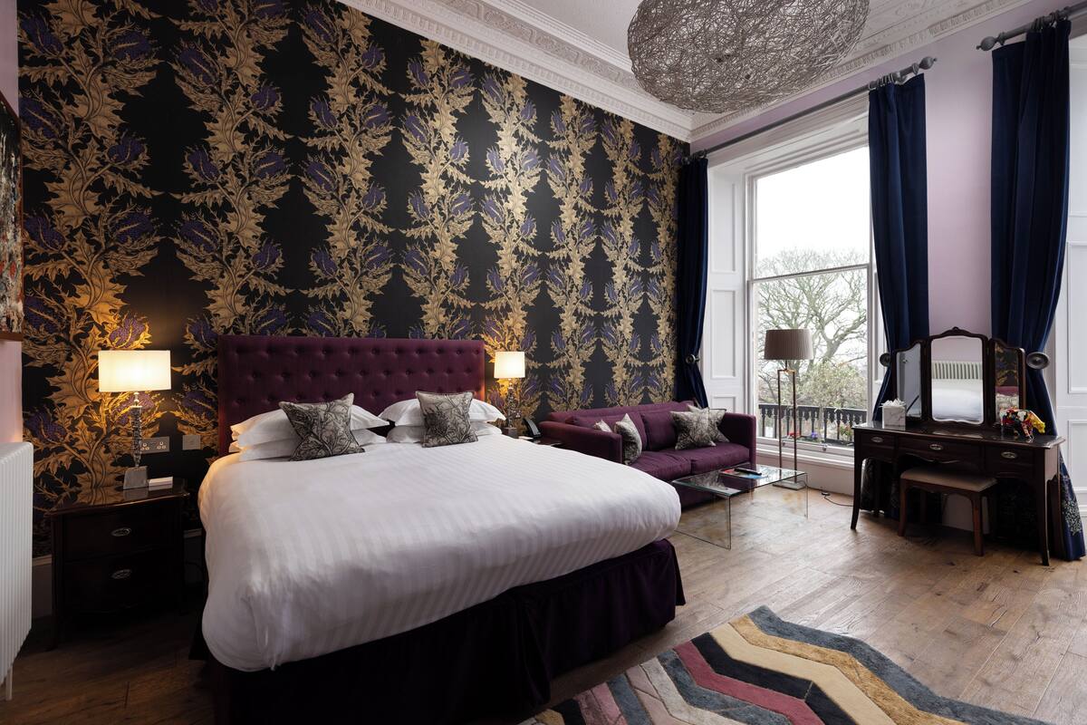 A bedroom with a large bed, a sofa, a dresser, and a window with curtains.