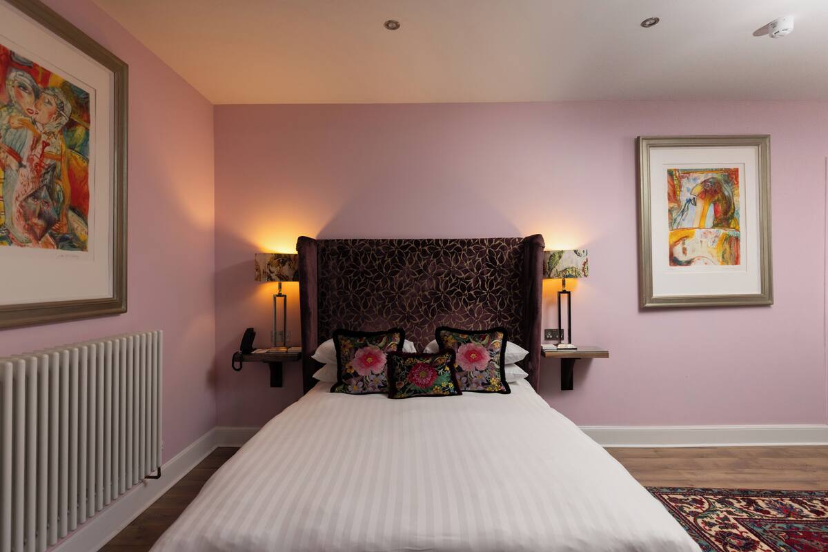 A neatly made bed with floral pillows, a patterned headboard, and wall-mounted lamps.