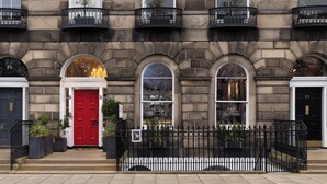 Un bâtiment avec une porte rouge, portant le numéro 24, et une enseigne indiquant la présence d’une galerie d’art et de jardins avec bar.