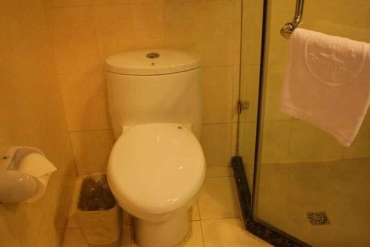A bathroom with a toilet, a trash bin, and a glass shower enclosure.