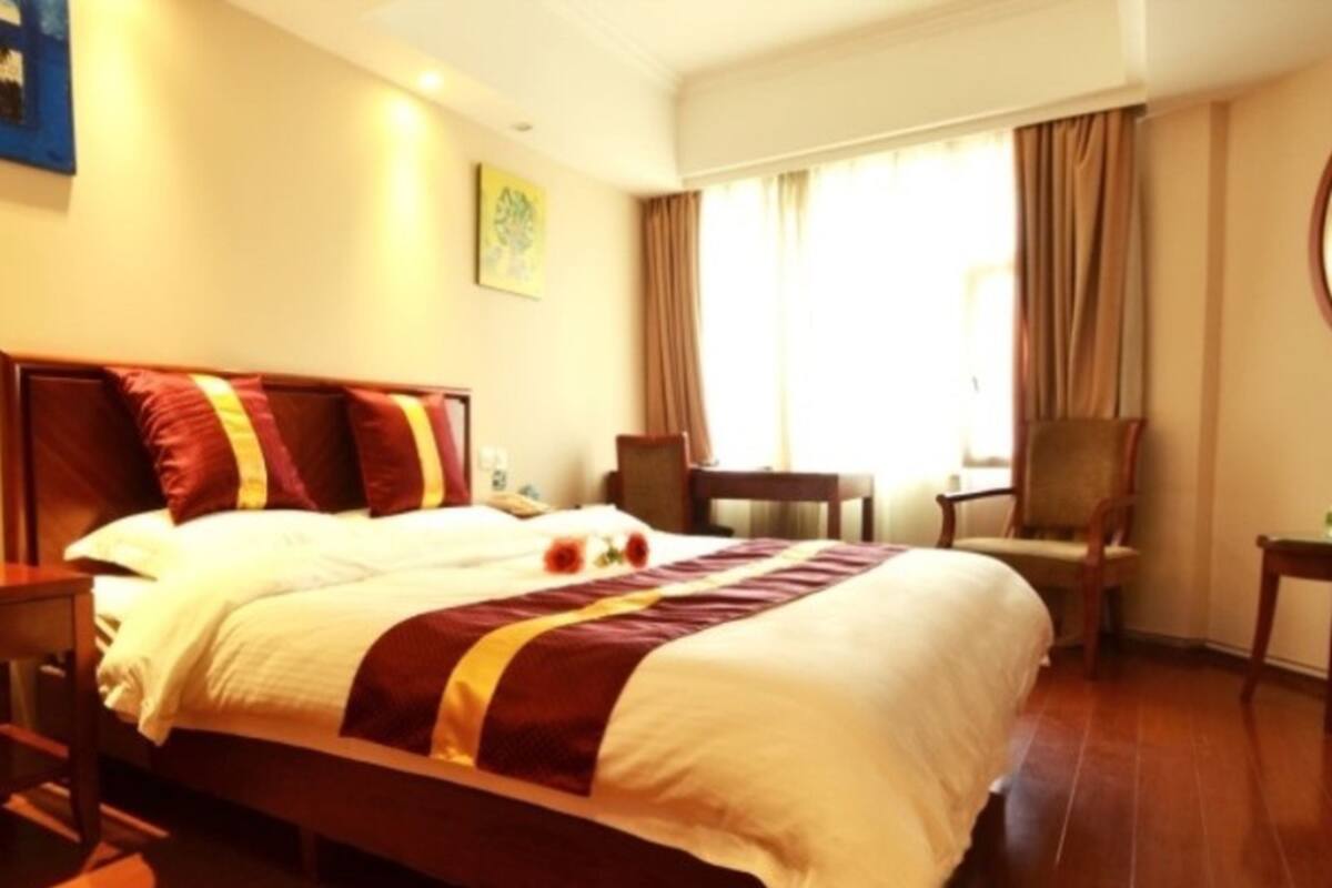 A hotel room with a large bed, a desk, two chairs, and a window with curtains.