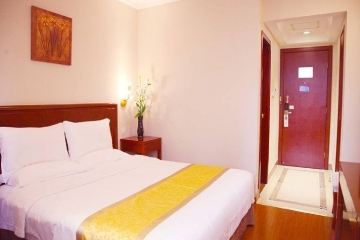 A hotel room with a bed, a nightstand with a vase of flowers, and a door.