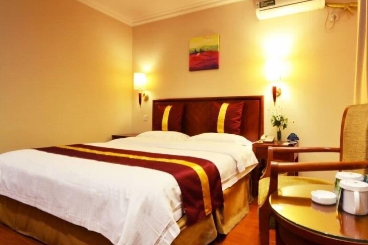 A hotel room with a bed, bedside table, chair, and a small table with a coffee maker.