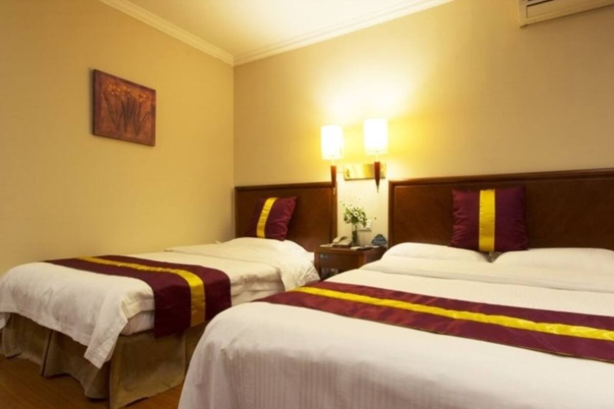 A hotel room with two single beds, a nightstand with a lamp, and a wall-mounted artwork.
