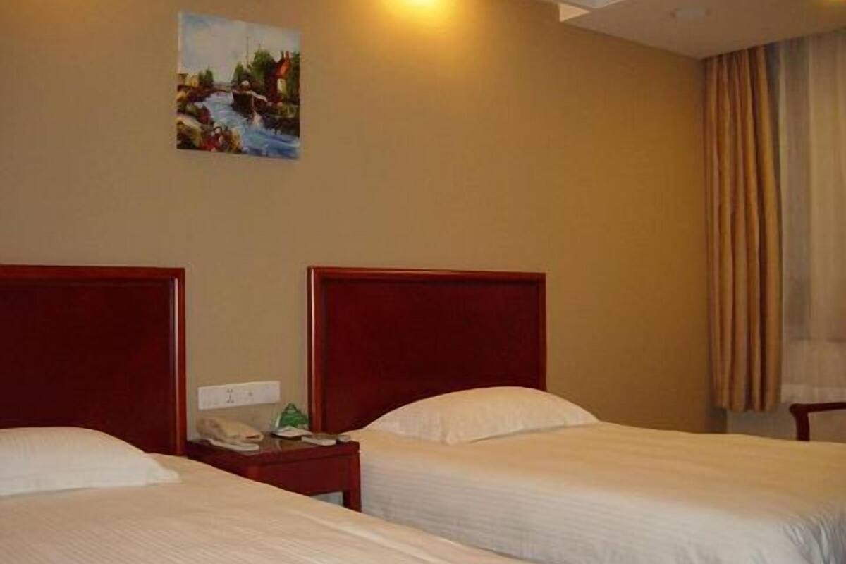A hotel room with two single beds, a nightstand with a phone, and a painting on the wall.