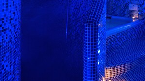 Een kamer met wandtegels in mozaïek en een vloeiend ontwerp, met een badkuip en een klein tafeltje met verlichting.