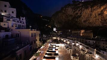 A rooftop terrace with outdoor seating and a view of a coastal town at night.