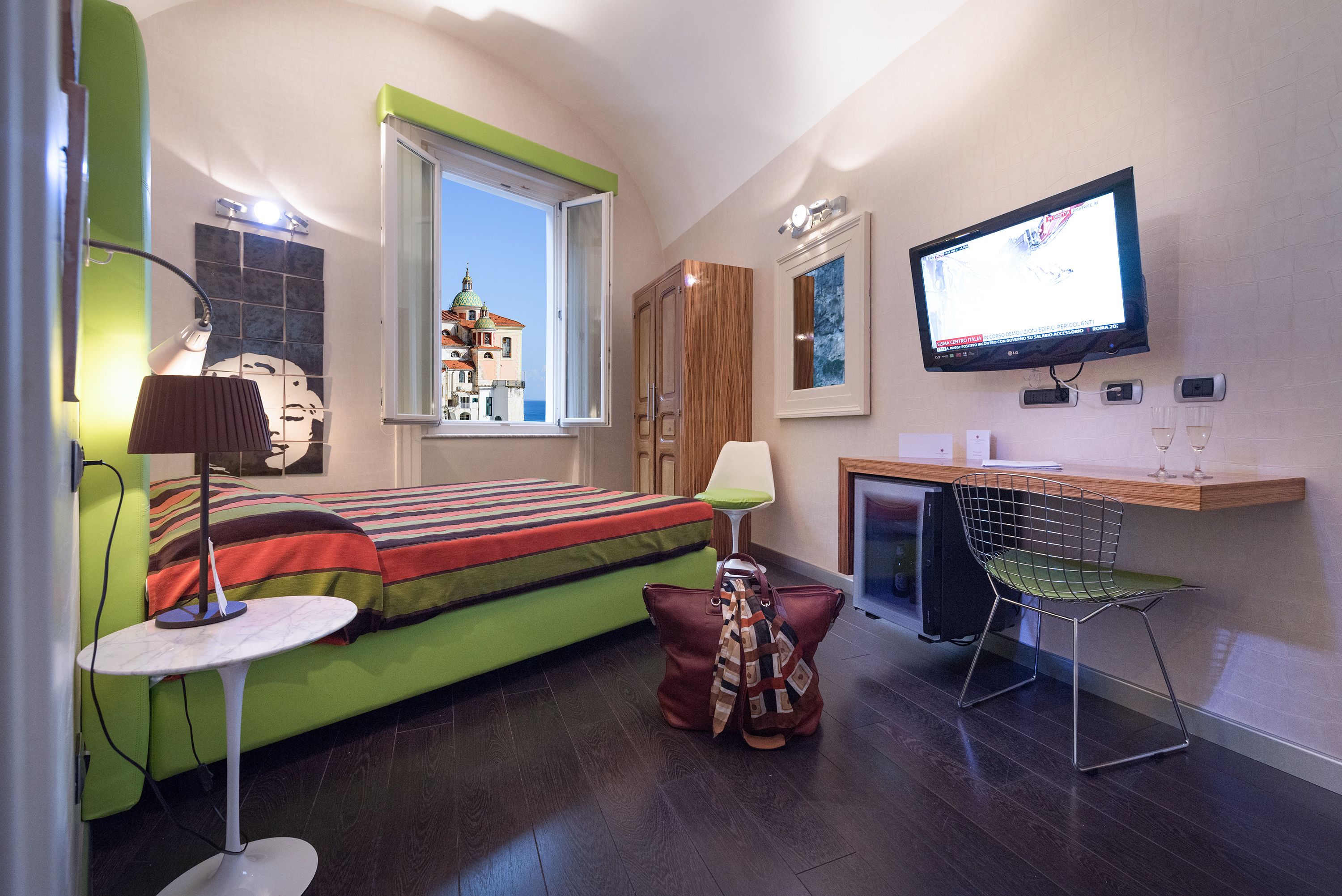 A compact room with a bed, a desk, a chair, a TV, and a window with a view of a building.