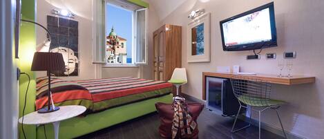 A compact room with a bed, a desk, a chair, a TV, and a window with a view of a building.