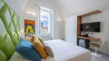Habitación de hotel moderna con un cabecero tapizado en verde, una cama con varias almohadas, un escritorio y un televisor de pantalla plana, además de un ventanal con vistas a la ciudad.