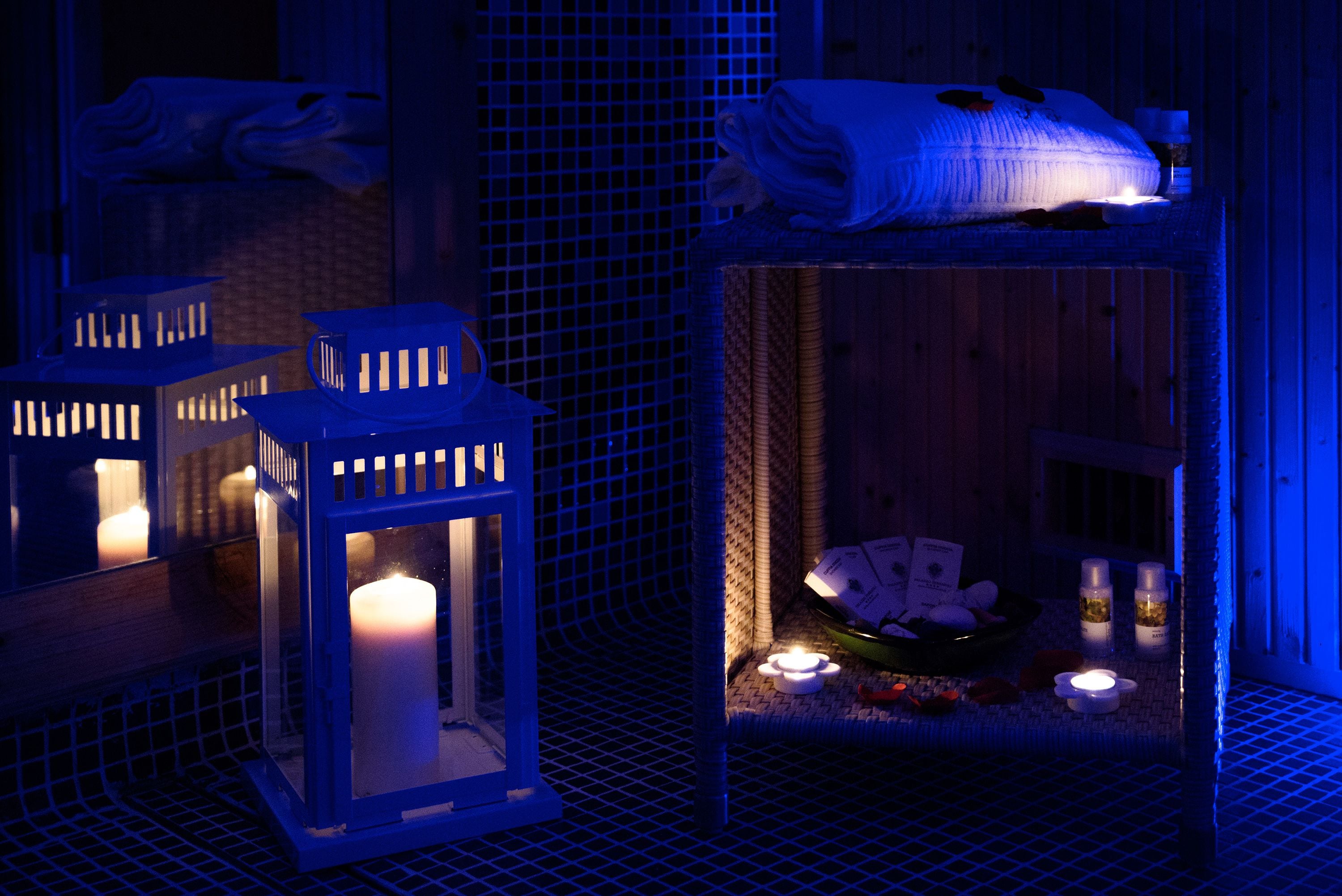 Zona de spa con un banco de madera, velas y un estante pequeño con botellas.