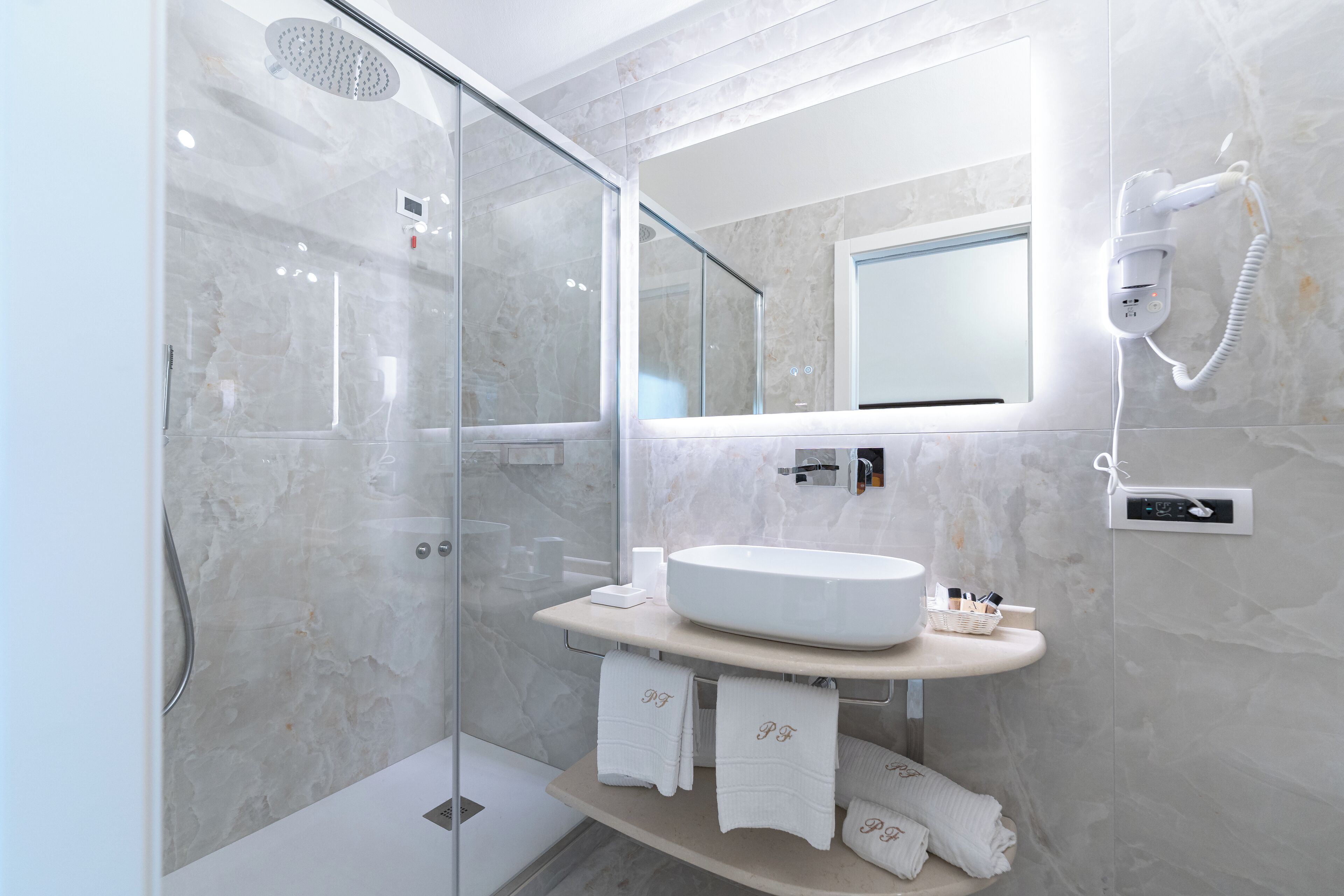 A modern bathroom with a glass-enclosed shower, a large mirror, and a white sink with a marble countertop.