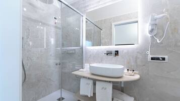A modern bathroom with a glass-enclosed shower, a large mirror, and a white sink with a marble countertop.