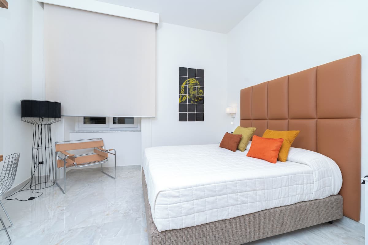 Un dormitorio moderno con una cama grande, un banco, una lámpara de pie y una obra de arte en la pared.