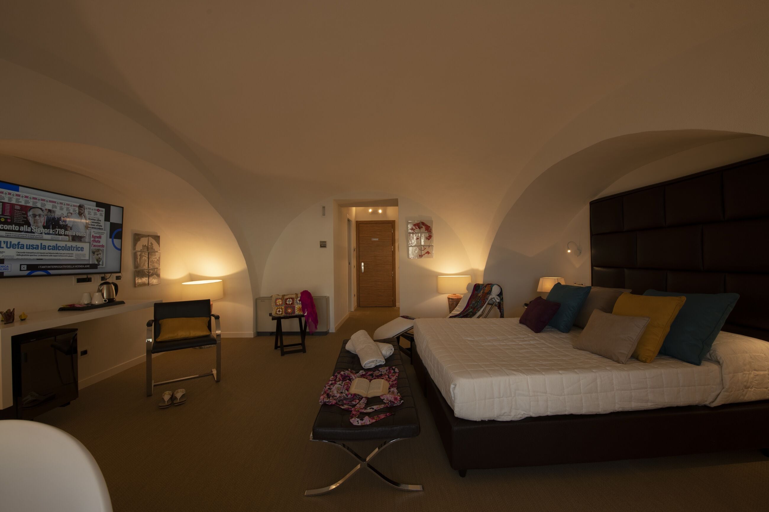 Habitación de hotel con cama, escritorio, silla, televisión y una pequeña mesa con lámpara.