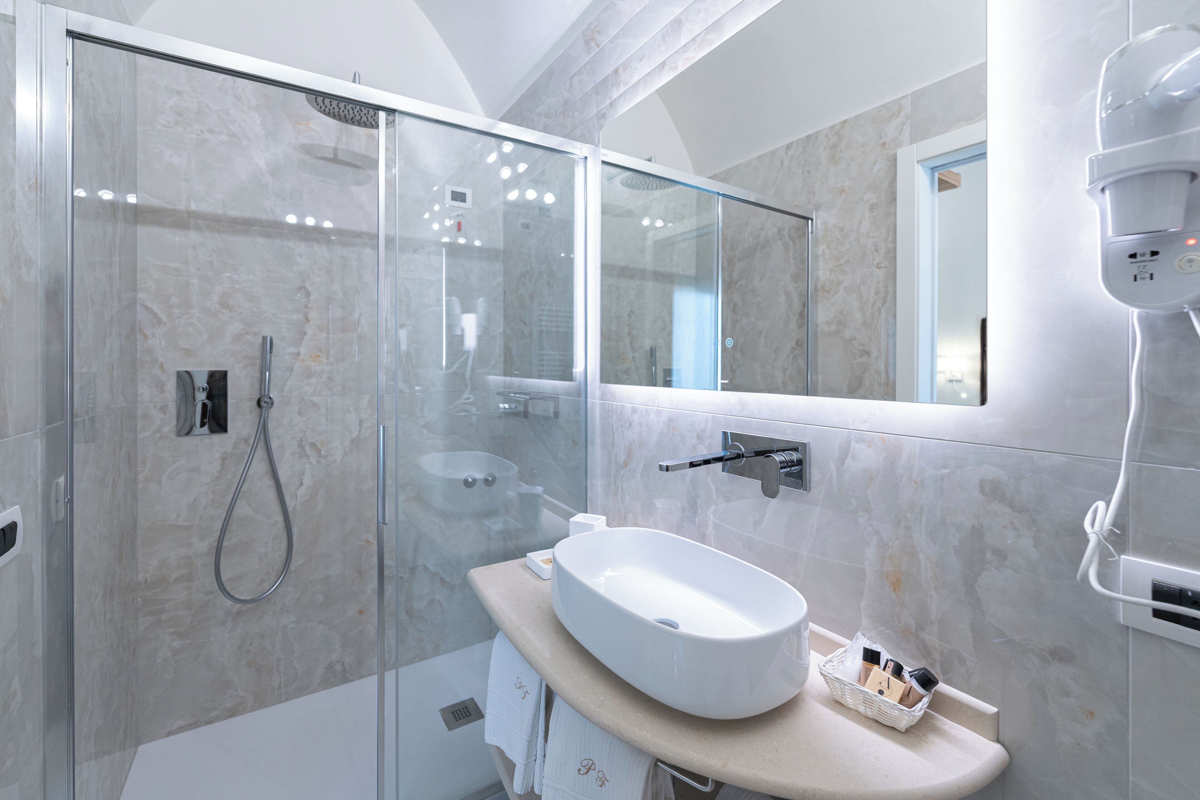 Un bagno moderno con doccia vetro, lavandino bianco e specchio.