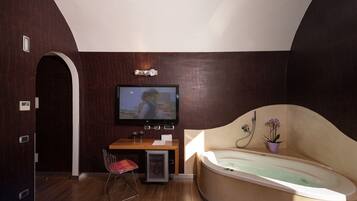 A modern bathroom with a large bathtub, a television mounted on the wall, and a small seating area with a chair and a table.