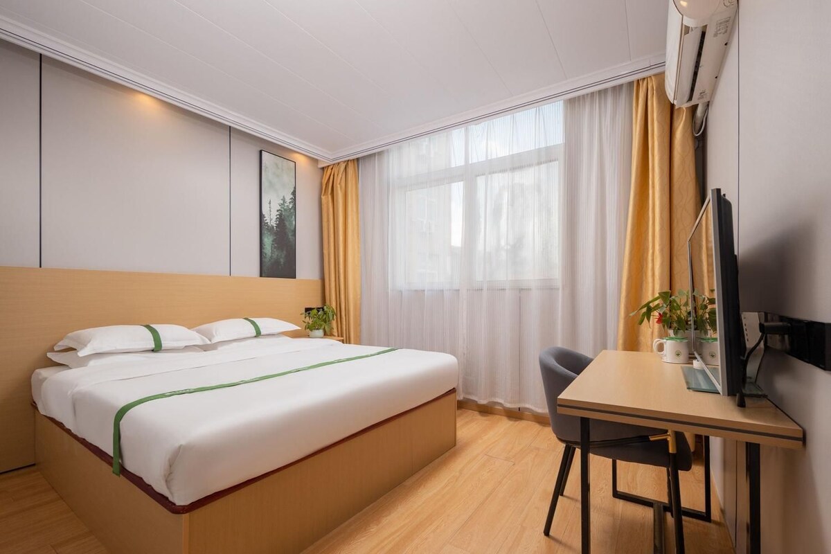 A hotel room with a bed, a desk, a chair, a television, and a window with curtains.
