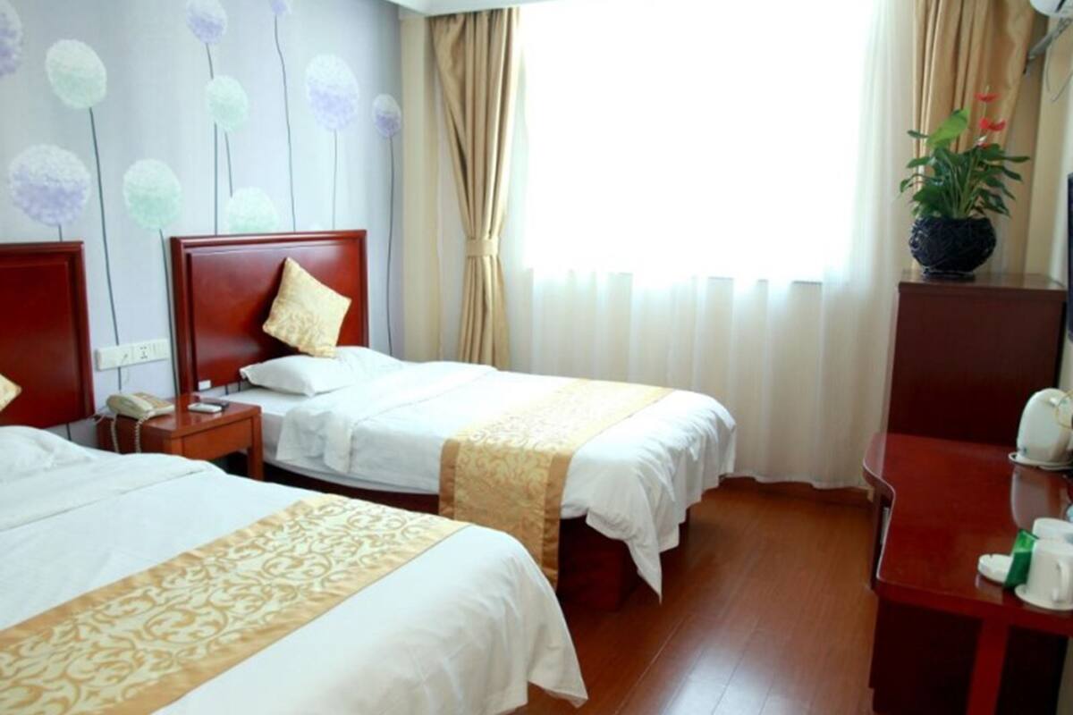 A hotel room with two beds, a wooden floor, a desk with a telephone, and a potted plant.