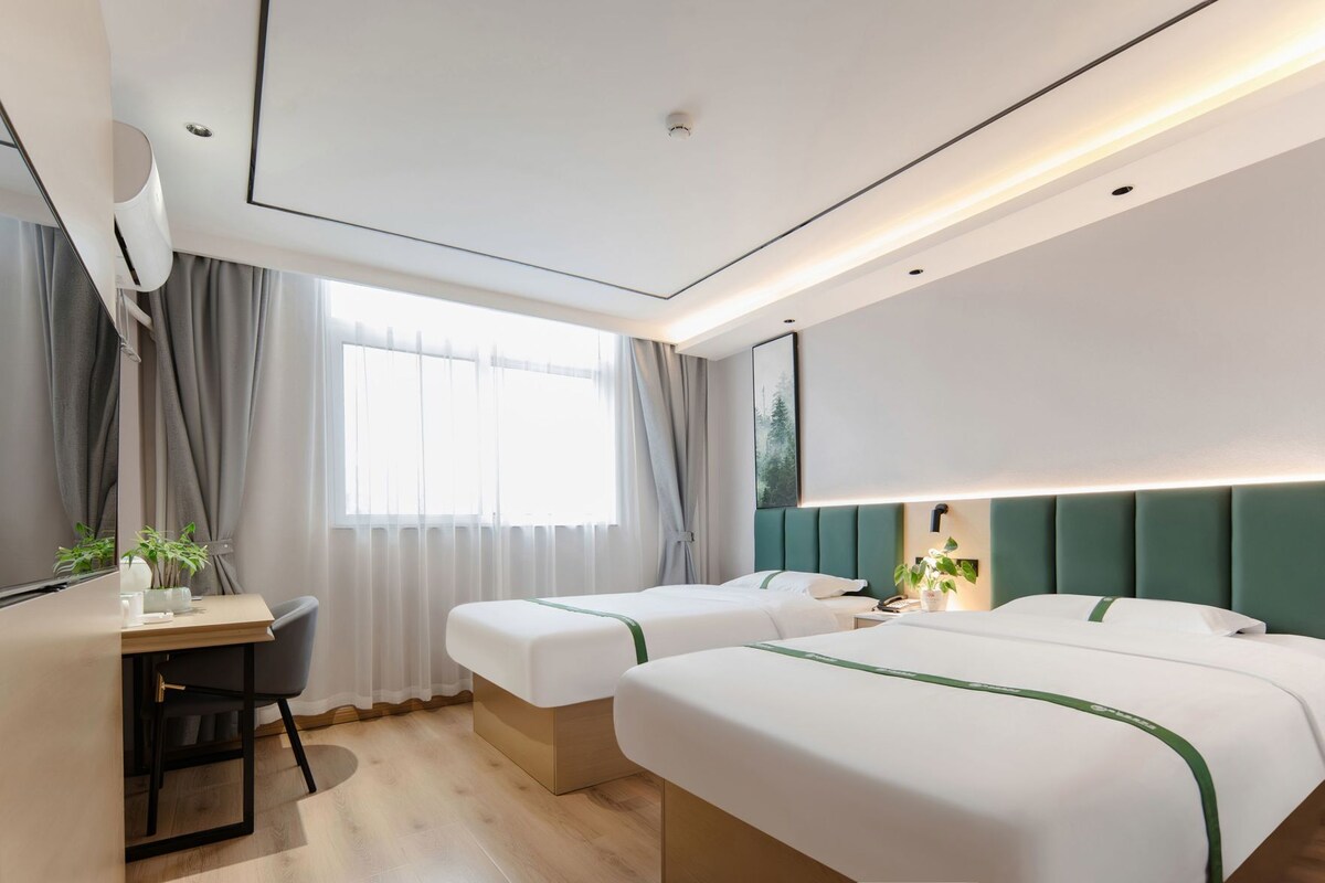 A hotel room with two beds, a desk, and a window with curtains.