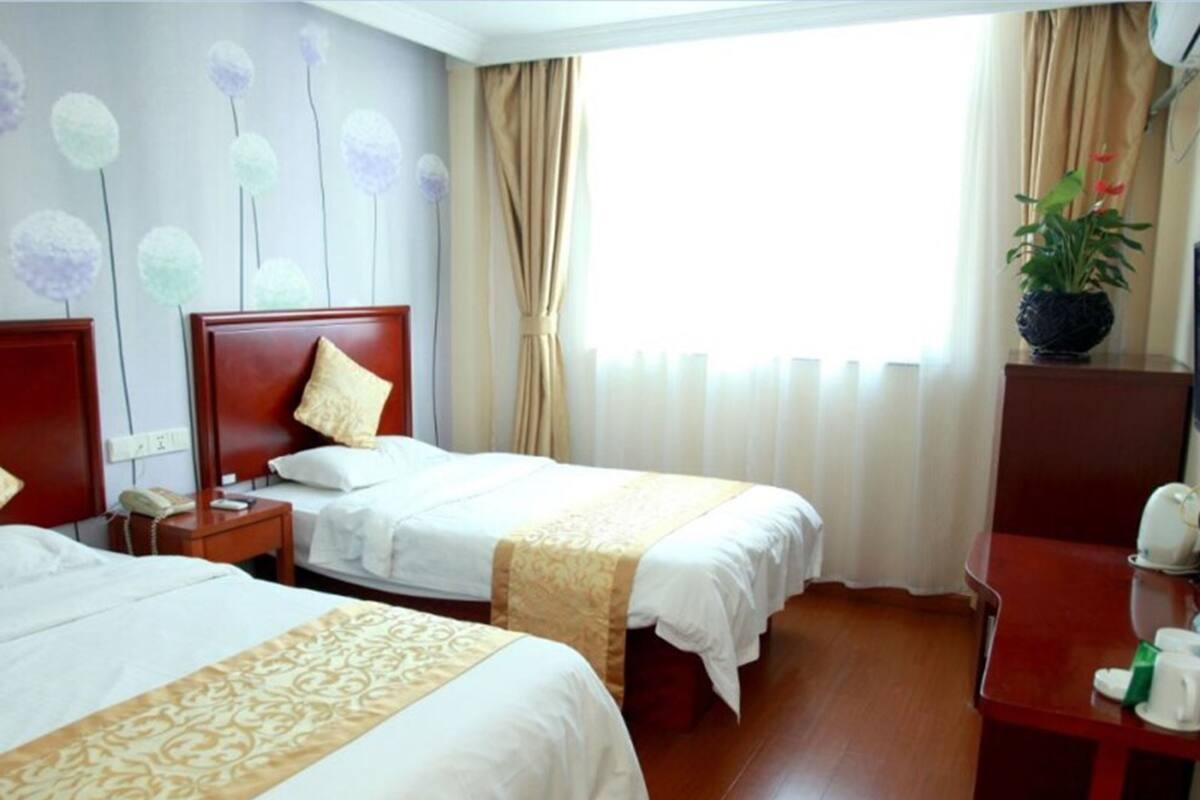 A hotel room with two beds, a wooden floor, a desk with a telephone, and a window with curtains.