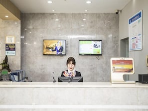 A reception desk with a computer, a television, and a digital information board.