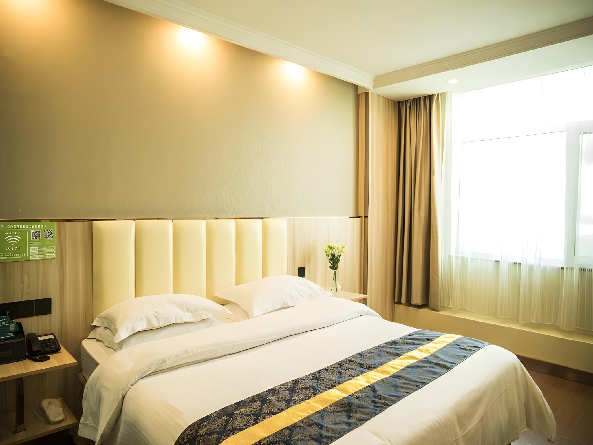 A hotel room with a large bed, a bedside table with a lamp, a phone, and a window with curtains.