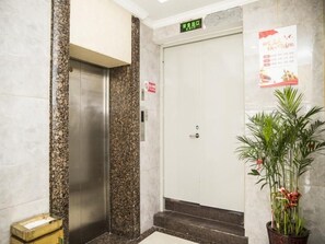 Ein Aufzug in einer Lobby mit Marmorwand, Blumentopf und einem Schild über der Aufzugtür.
