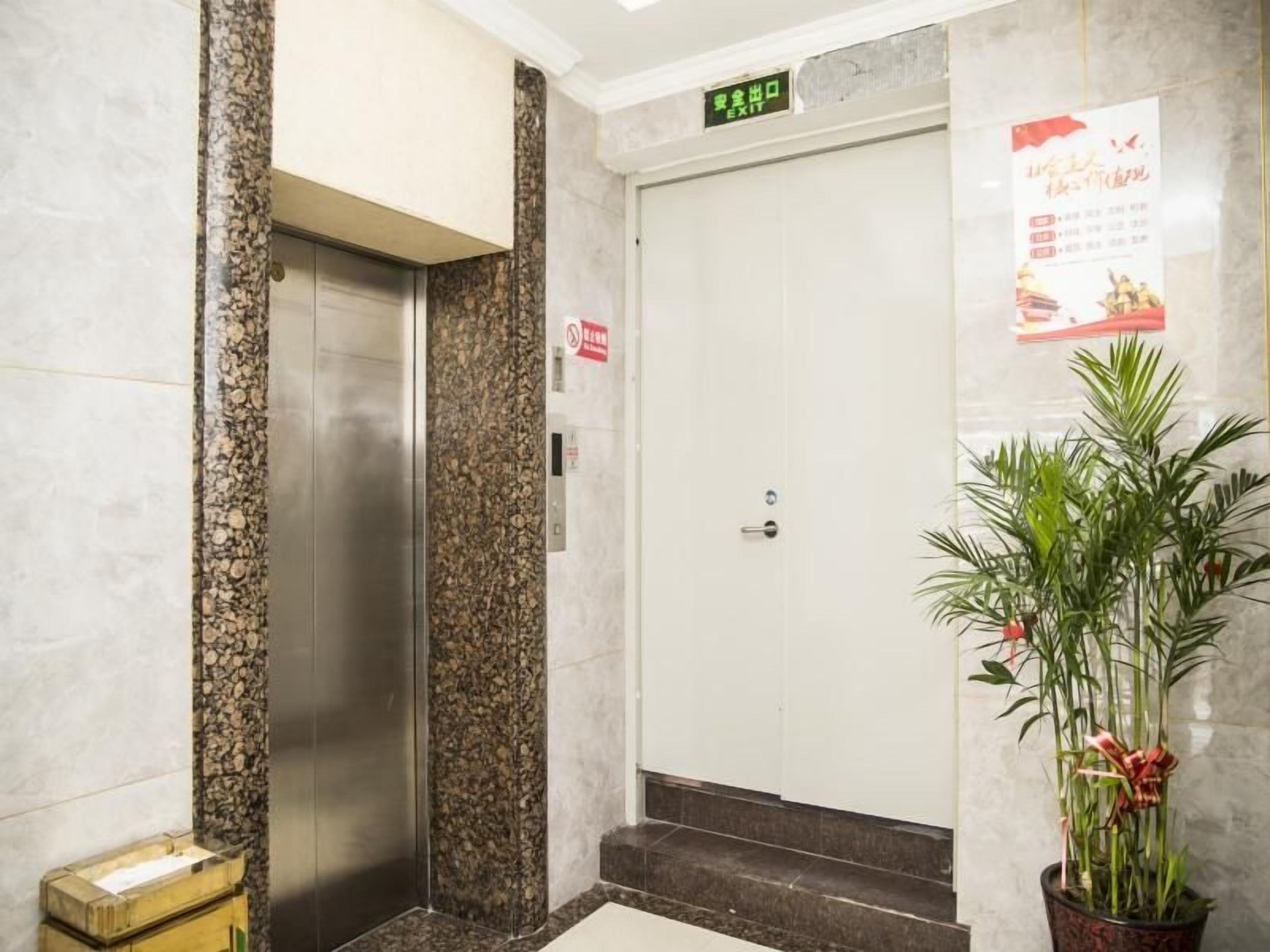An elevator in a lobby with a marble wall, a potted plant, and a sign above the elevator door.