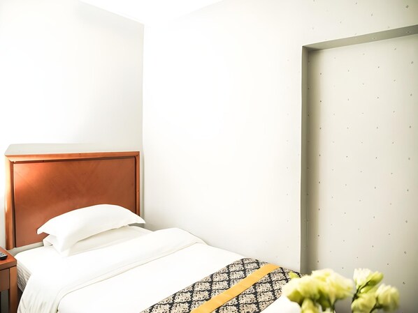 Une chambre d’hôtel avec une tête de lit en bois, une couvre-lit blanche et un plaid à motifs.