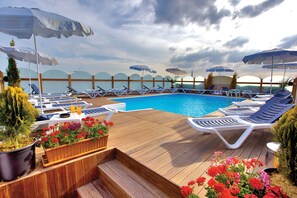 Zona junto a la piscina con sillones de descanso, sombrillas y plantas en macetas.