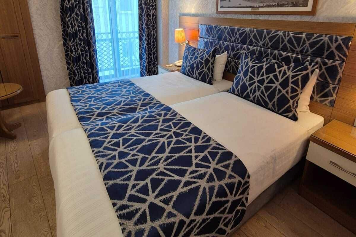 A hotel room with a large bed, a nightstand, a lamp, a window with curtains, and a picture on the wall.