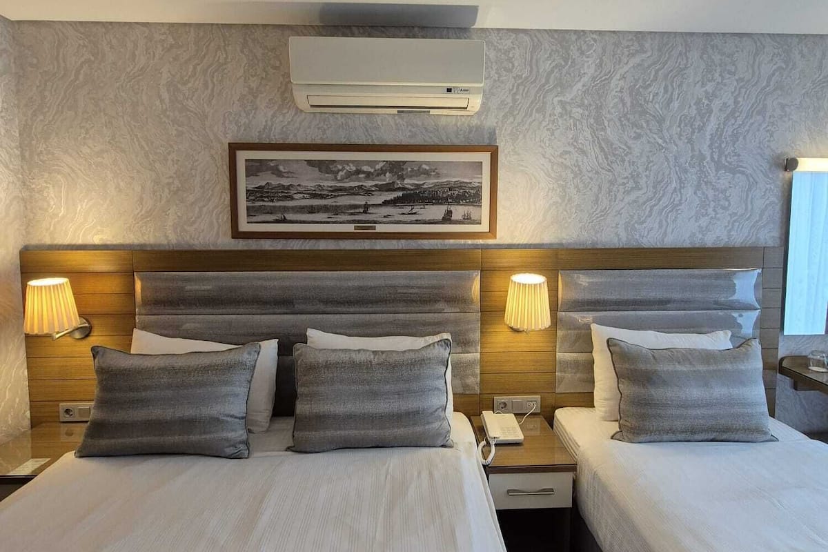 A hotel room with two beds, a mounted air conditioner, a framed picture on the wall, and bedside lamps.