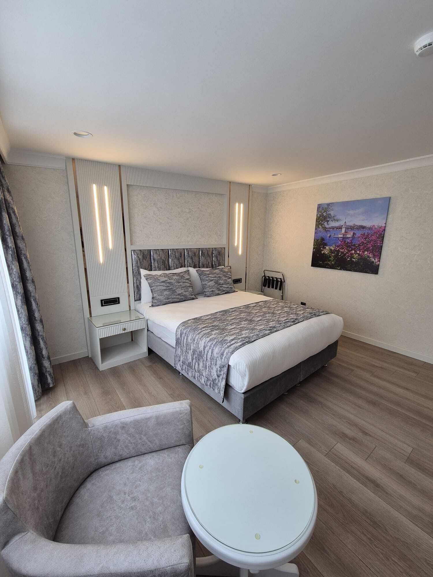 Una habitación de hotel moderna con cama, mesita de noche, silla y una pequeña mesa redonda.