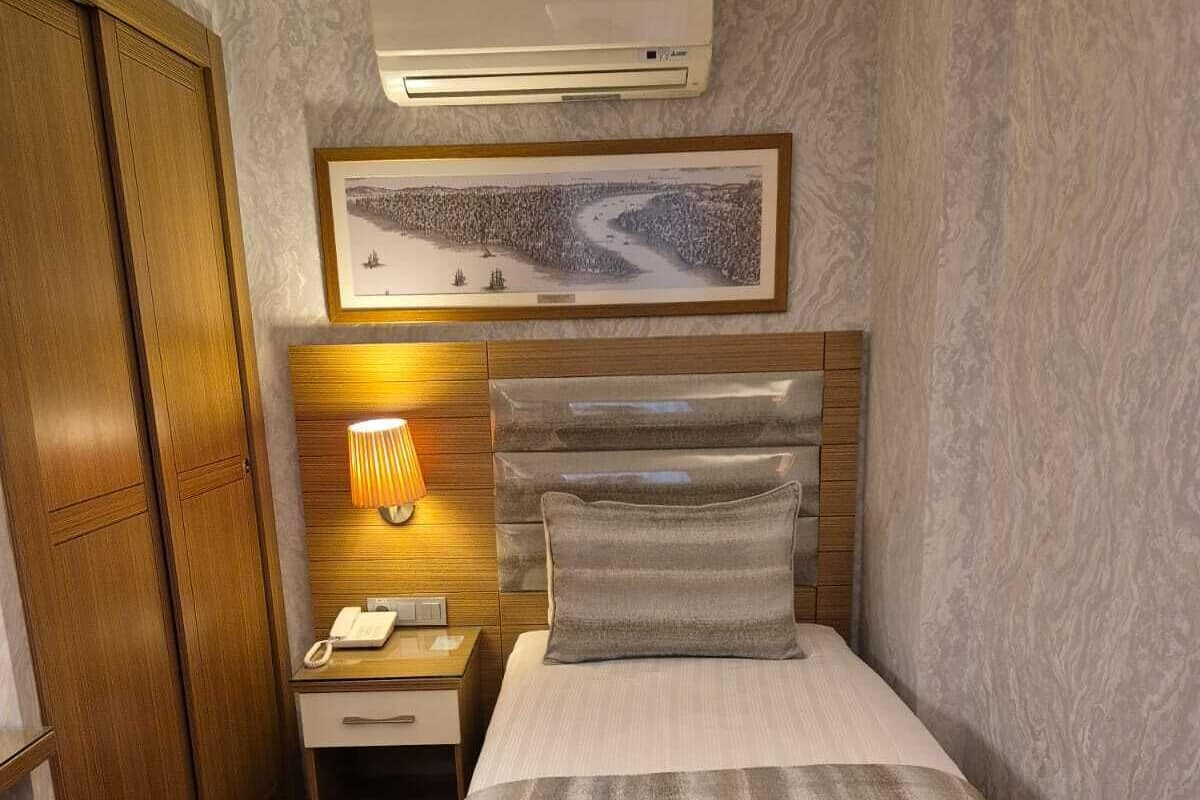 A hotel room with a bed, a nightstand with a lamp, a telephone, a picture on the wall, and an air conditioning unit.
