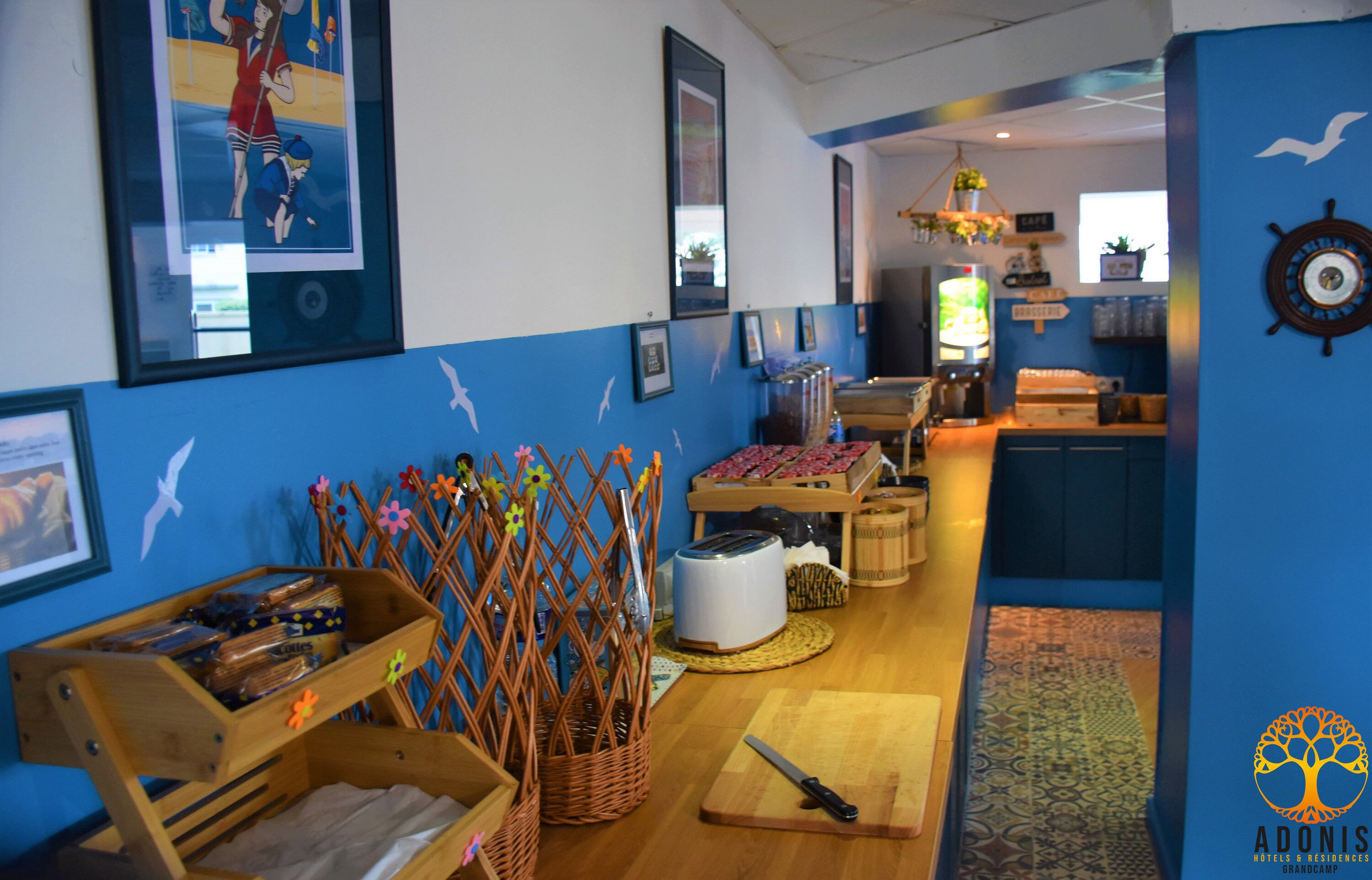 A hotel lobby with a nautical theme, featuring a wooden reception desk, a coffee machine, and framed artwork on the walls.