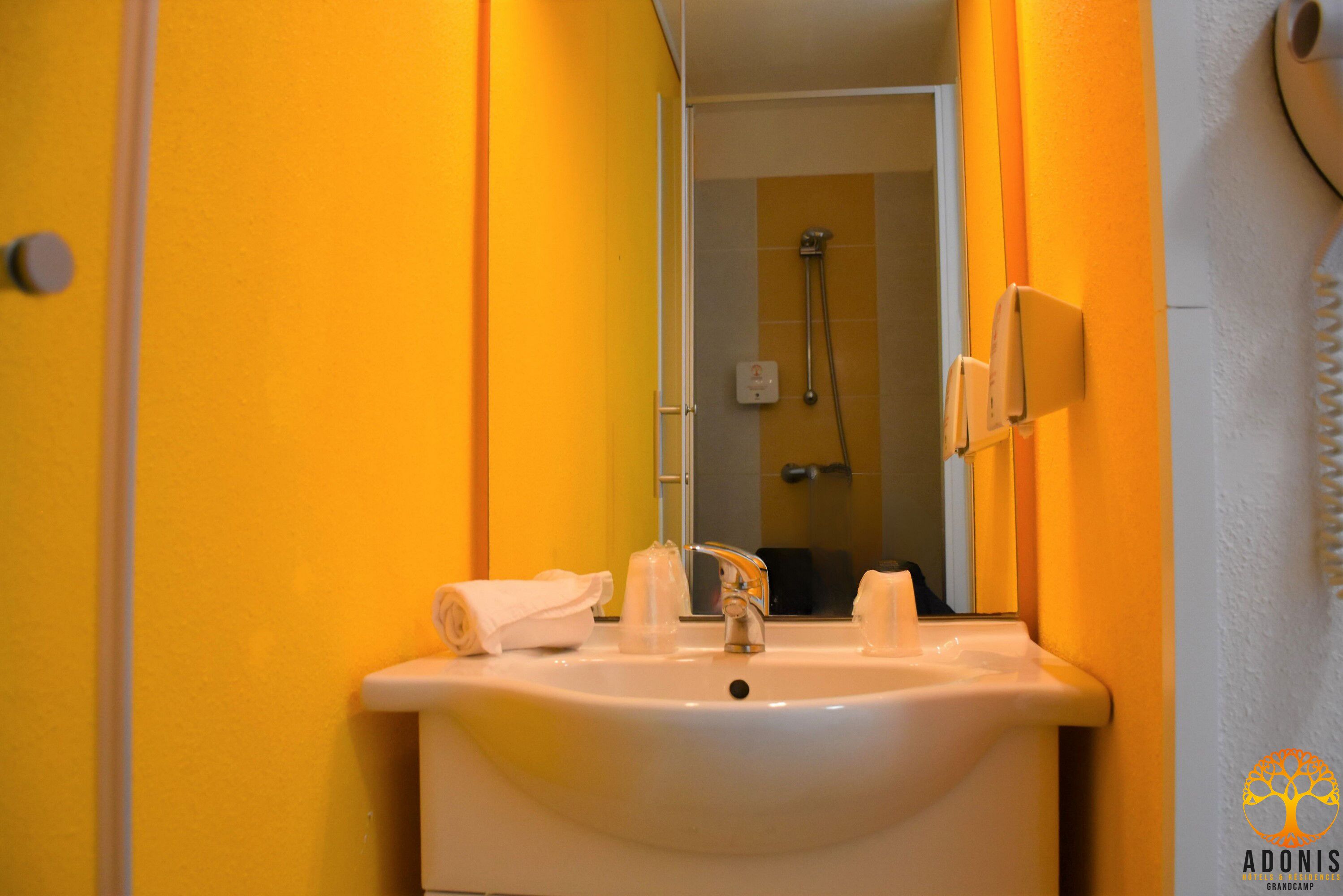 A bathroom with a white sink, a mirror, and a shower visible in the background.