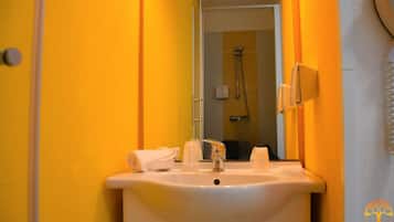 Un baño con un lavamanos blanco, un espejo y una ducha a la vista.