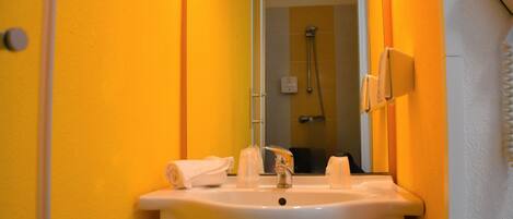 A bathroom with a white sink, a mirror, and a shower visible in the background.