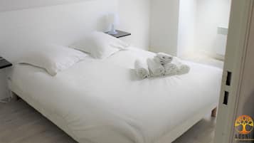 Un lit bien fait, avec du linge de lit et des serviettes blanches, une table de chevet avec une lampe, et une chambre au design moderne et minimaliste.
