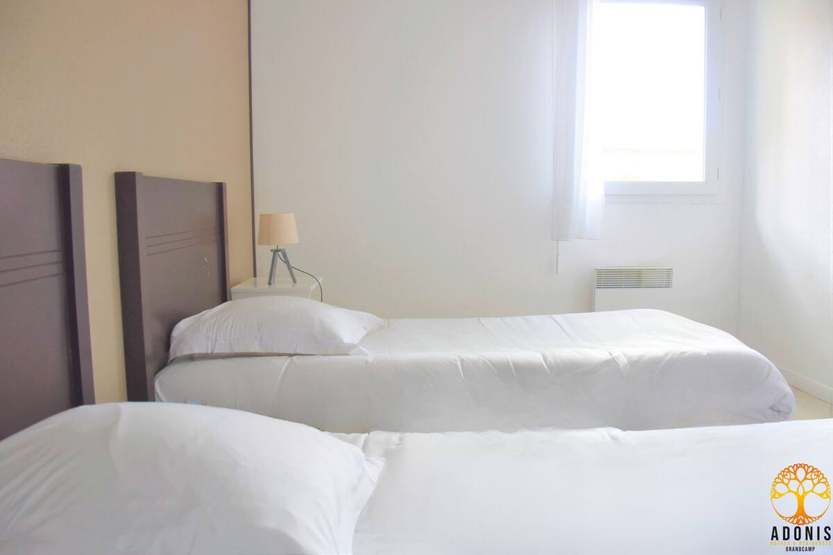 Habitació d'hotel amb dos llits individuals, una taula de nit amb una làmpada i una finestra amb persianes.