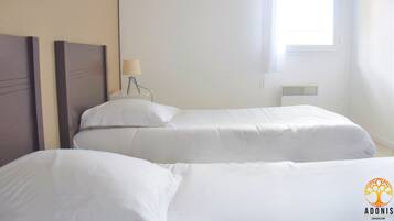 A hotel room with two single beds, a bedside table with a lamp, and a window with blinds.