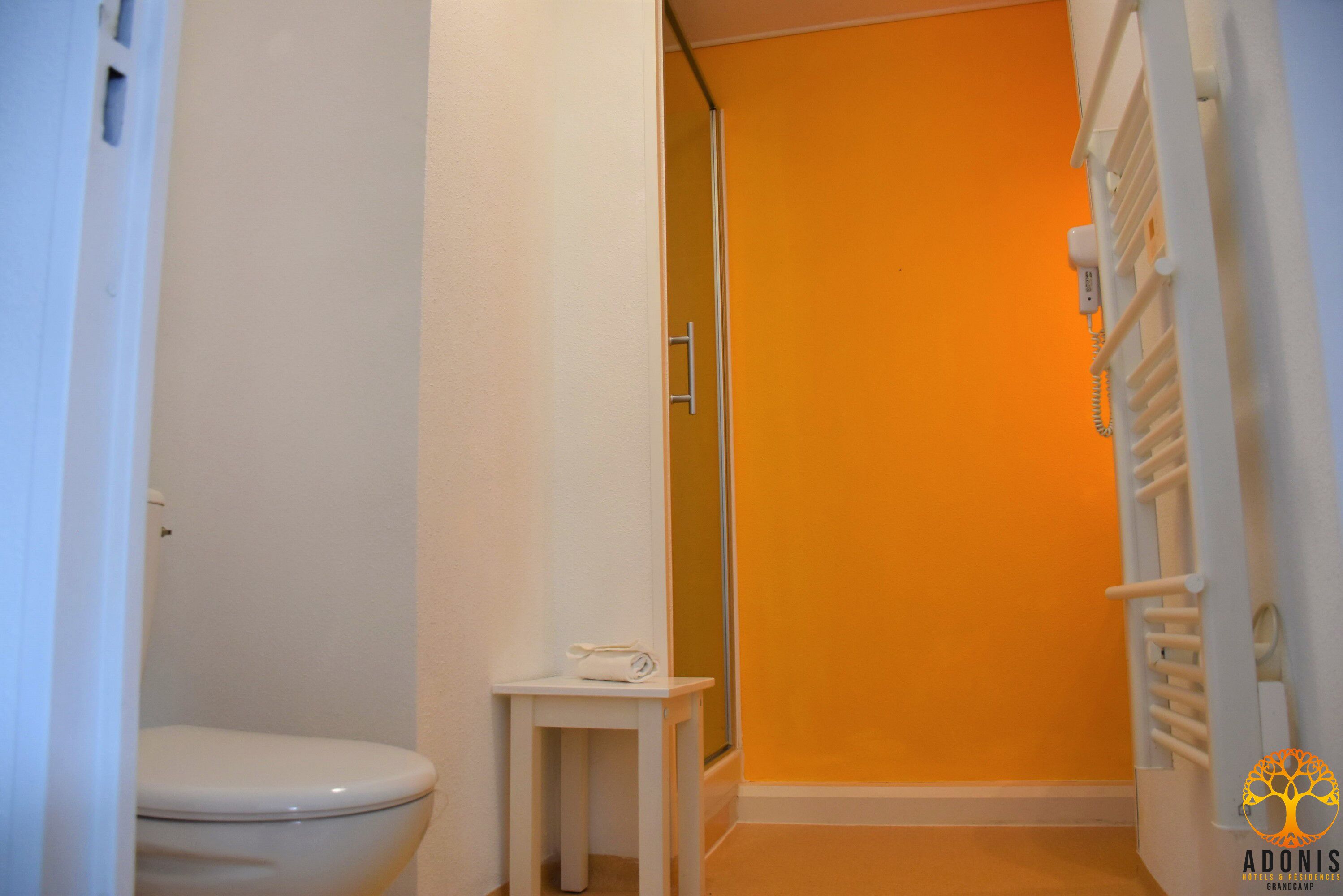 Un baño con inodoro, una mesita con una toalla y zona de ducha.